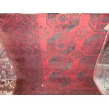 An Afghan wool carpet, the black geometric detail upon a mid red ground, within alternating