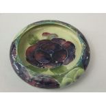 A Moorcroft dish of circular form with curved rim and purple pansy detail on a green ground and