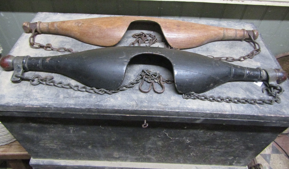 Two similar carved wooden yokes complete with hooks and chains