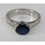 An 18ct white gold ring set with an oval sapphire and channel set diamond shoulders, size M, 4.3g