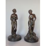 Two similar cast bronze figural study of semi-nude ladies upon stepped circular black slate bases,