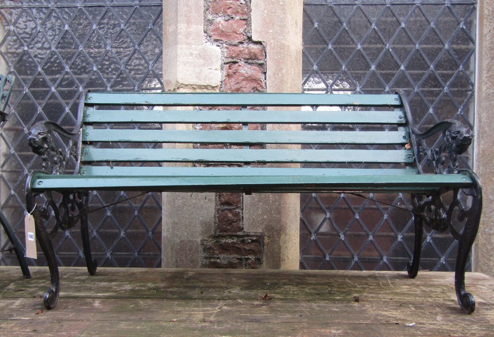 A three seat garden bench with green painted timber lathes raised on a pair of cast iron end
