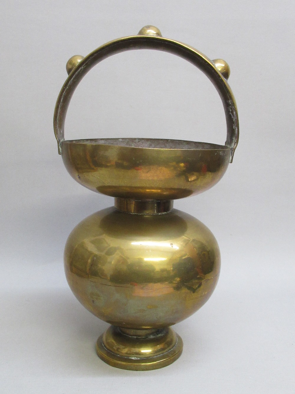 BRASS BALUSTER SHAPED VESSEL ON A SMALL PEDESTAL FOOT WITH HOOP HANDLE ORNAMENTED BY THREE APPLIED