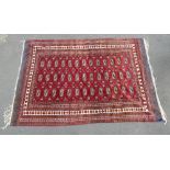 PAKISTANI BOKHARA PATTERN RUG, THE MADDER FIELD WITH THREE ROWS OF OCTAGONS SURROUNDED BY A MULTIPLE