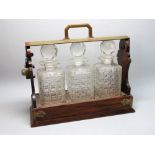 EDWARDIAN ROSEWOOD TANTALUS WITH METAL MOUNTS CONTAINING THREE CUT GLASS DECANTERS WITH FACETED