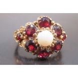 9ct GOLD FLORAL RING SET 8 x 4mm GARNETS ENCLOSING A CIRCULAR 6mm WHITE OPAL, SIZE O½ (6.5g GROSS)