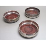 SET OF THREE SILVER MOULDED CIRCULAR WINE COASTERS, EACH WITH A TURNED MAHOGANY BASE, BY