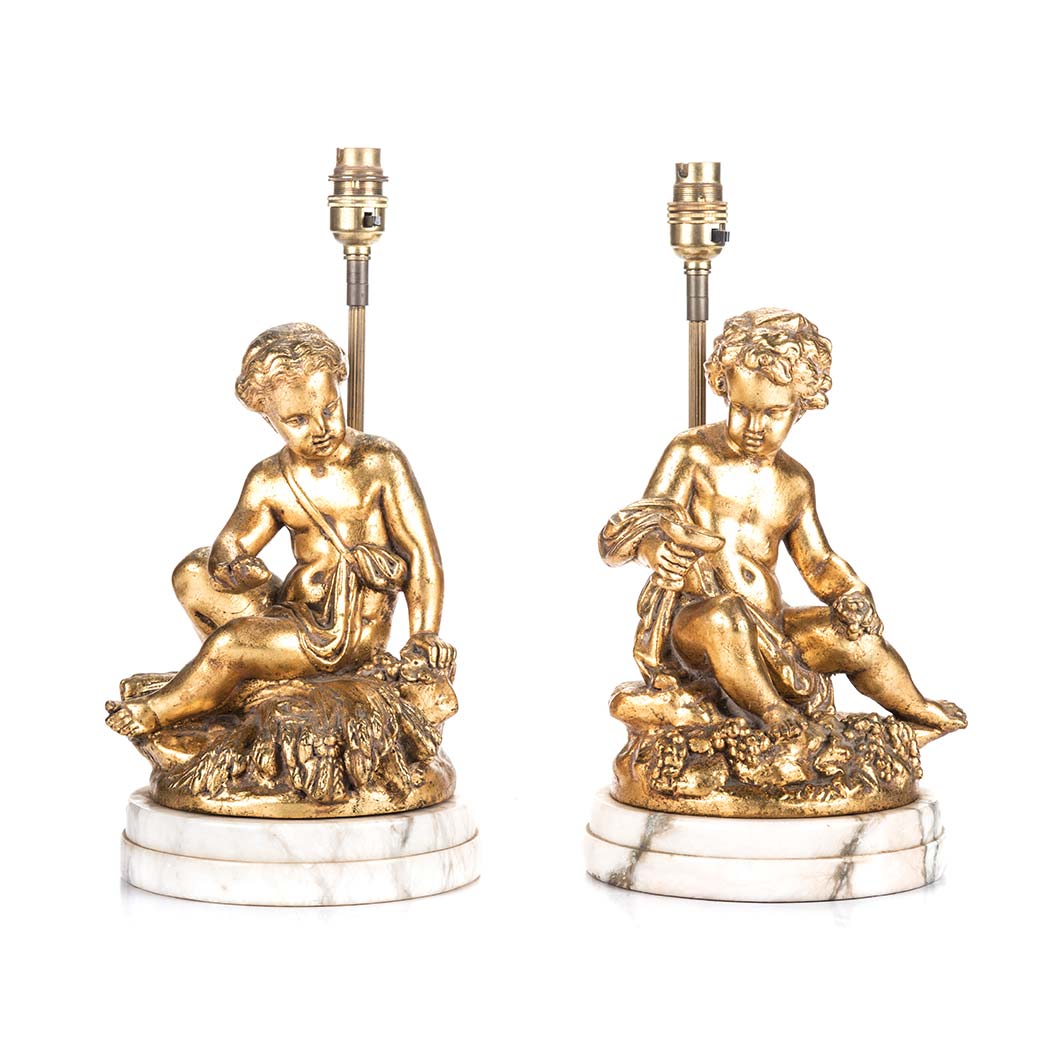 A PAIR OF GILDED METAL LAMPS, 19TH CENTURY each decorated with cherubs sitting on a bail of wheat,