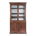 A TEAK CUPBOARD BOOKCASE in two parts, the outswept cornice above a plain frieze, a pair of glazed
