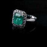 AN EMERALD AND DIAMOND RING The central emerald cut emerald is claw set and surrounded by pave set