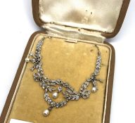 An Edwardian pearl and diamond necklace, in a bow and leaf design, with four pearl drops, on a white