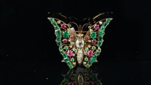 An antique, emerald, ruby and diamond butterfly brooch. cushion shaped central diamond, the