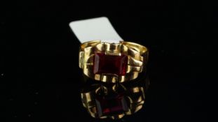 Synthetic ruby ring, rectangular step cut synthetic ruby in a yellow metal surround, with scroll