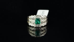 Emerald and diamond ring, central step cut emerald with round brilliant cut diamond detail, in white