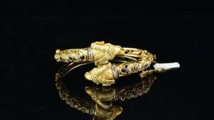 A gold sapphire and diamond bangle, designed as two rams heads in a crossover position, set with