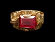 Synthetic ruby ring, rectangular step cut synthetic ruby in a yellow metal surround, with scroll