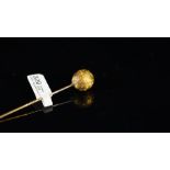 Yellow metal stick pin, set with an engraved sphere, tested as 18ct, length approximately 85mm