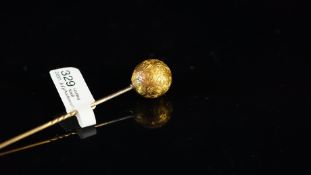 Yellow metal stick pin, set with an engraved sphere, tested as 18ct, length approximately 85mm
