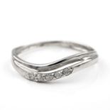 A diamond set ring. The ring designed as a shaped polished band, set to the front with a row of