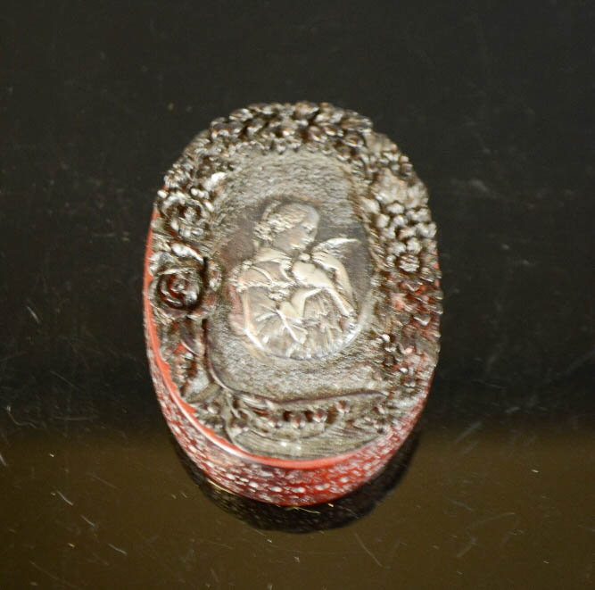 An oval Paris resin trinket box, signed, with relief moulded girl holding a dove to the lid. 7cm
