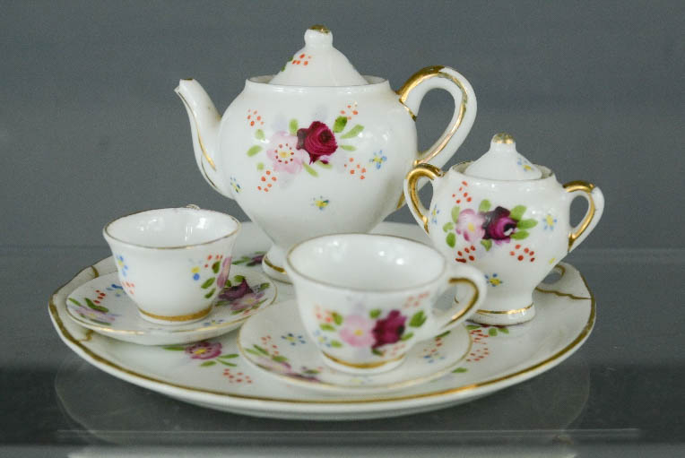 An antique porcelain miniature tea service, painted with flowers and having gilt decoration.