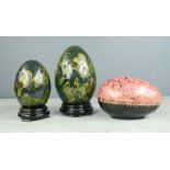 Two hand decorated Chinese eggs on stands, and a papier mache egg form trinket box.