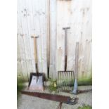 A group of garden tools, including shovel, pick axe, fork, hay fork and saw.