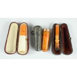 Three cheroot holders, one in amber with 9ct gold rim and silver travelling case, the other two with