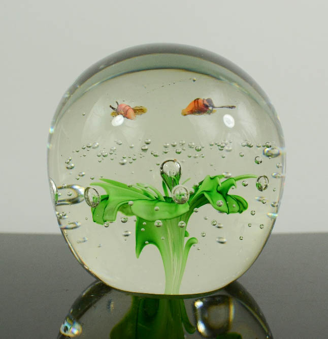 A Murano glass paperweight with green flower and two bees.