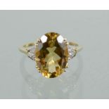 A 9ct gold and oval cut yellow topaz ring, flanked with three white paste stones to the shoulders,