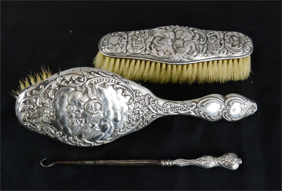 A silver clothes brush, hair brush, and button hook, embossed with cherubs.