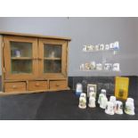 A miniature pine cabinet with two glass doors containing a collection of thimbles.