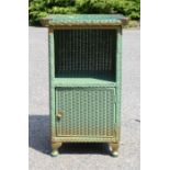 A green Lloyd Loom bedside table with glass top.