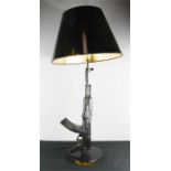 A lamp in the form of a machine gun, with black shade and gilt interior.