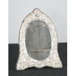 A silver embossed mirror, the oval bevelled mirror plate bordered by a decorative silver frame of