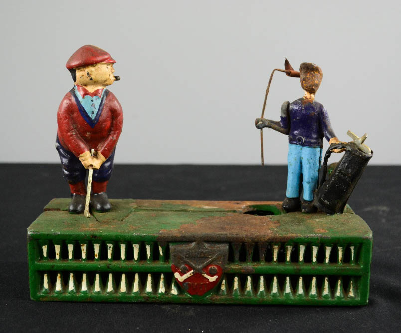 An antique painted metal money box with golfing figures to the top.