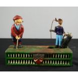 An antique painted metal money box with golfing figures to the top.