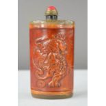 An ox horn Chinese carved snuff bottle with dragon design and red jade stopper.