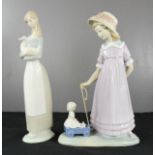 A Lladro girl pulling toy cart and a Nao figurine.