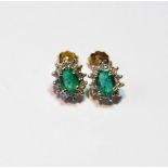 Pair of diamond and emerald oval cluster ear studs.
