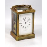 Brass repeating carriage clock mounted by a loop handle over white enamelled face,