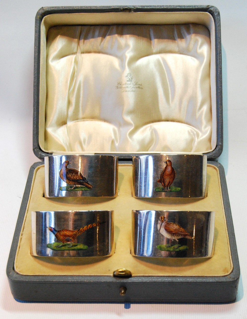 Set of four silver napkin rings, plain oval, each with an enamelled game bird, Chester 1923,