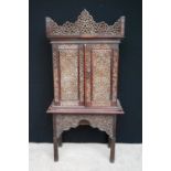 Siamese cabinet on stand with all over floral carving, sloped cornice over doors enclosing shelves,