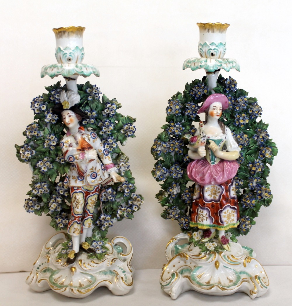 Pair of 18th century Chelsea Derby figural bocage candlesticks, he holding a cockerel,