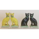 Two pairs of porcelain figures of cats on cushions, one pair yellow, the other pair black,