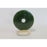 Green jade pierced disc set in a marble pebble base, 17cm diameter.