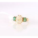 Yellow metal three-stone ring set with central opal flanked by two emeralds.