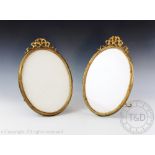 A pair of Edwardian gilt brass oval photograph frames, each with garland surmounts and easel backs,