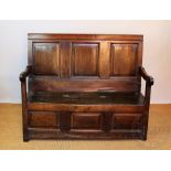 An 18th century oak settle, possibly Welsh, with three panel back above a hinge-top box seat,