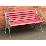 A cast iron and red painted wood garden bench, with floral and circular detailing to the sides,